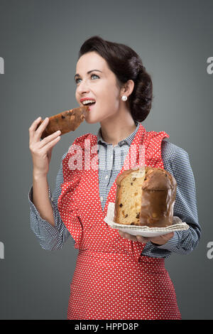 Vintage femme tablier en mangeant une tranche de panettone italien traditionnel, pâtisserie maison Banque D'Images