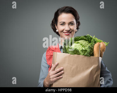 Smiling vintage femme tablier en tenant un sac de shopping. Banque D'Images