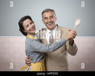 Smiling vintage couple en dansant dans la cuisine et tenant une cuillère en bois Banque D'Images