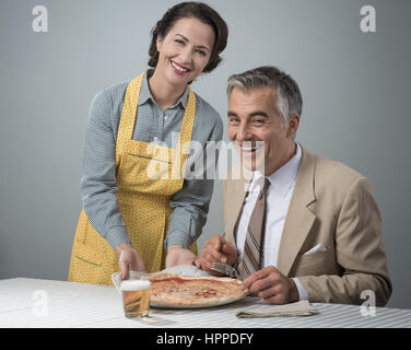 Happy vintage couple having dinner, elle est au service d'une pizza à son mari Banque D'Images