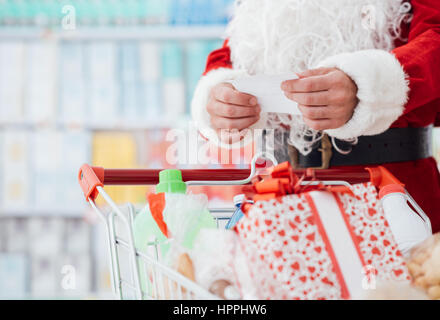 Père Noël faisant les courses au supermarché, il pousse un plein panier et contrôler une liste, Noël et shopping concept Banque D'Images