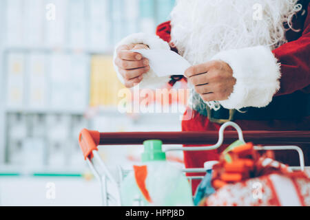 Père Noël faisant les courses au supermarché, il pousse un plein panier et contrôler une liste, Noël et shopping concept Banque D'Images