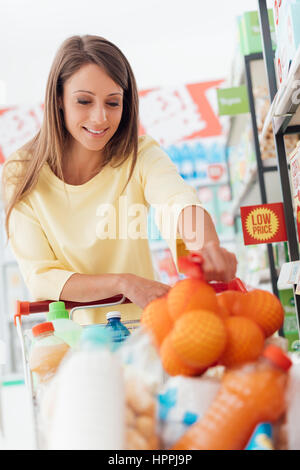 Jolie jeune femme faire les courses au supermarché, elle se met un sac en filet avec des oranges dans le chariot Banque D'Images