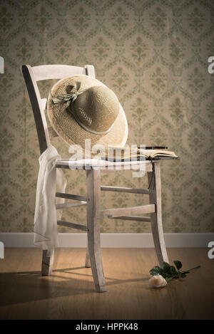 Vieux livre ouvert et chapeau de paille sur une chaise shabby chic et rose sur le sol. Banque D'Images