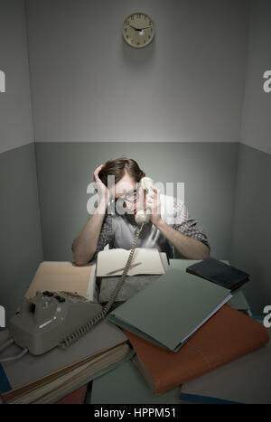 Retro geek au téléphone avec bureau malpropre dans une petite salle. Banque D'Images