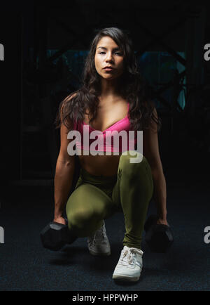 Sporty woman sitting with dumbbells sur fond de sport moderne. Entraînement avec haltères faire jeune fille maigre Banque D'Images