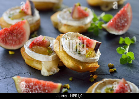 Épicé au four avec fromage de chèvre apéritifs crostini, figure la moutarde, pistaches et figues fraîches servi sur une ardoise board Banque D'Images