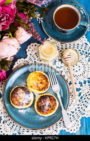 Beignets de fromage cottage, de miel et de thé dans une tasse d'époque sur un fond bleu. Studio Photo Banque D'Images