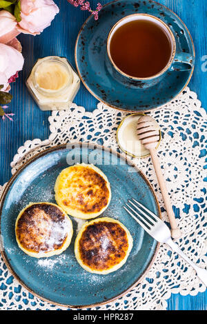 Beignets de fromage cottage, de miel et de thé dans une tasse d'époque sur un fond bleu. Studio Photo Banque D'Images