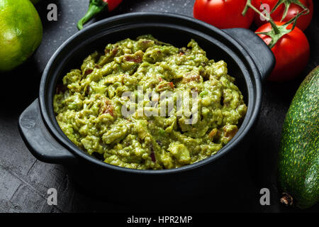 Bol de guacamole avec des ingrédients frais sur un tableau noir Banque D'Images