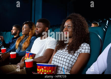 Entrer dans le monde de fiction. African woman smiling magnifiques tout en appréciant un film avec ses amis au cinéma Banque D'Images