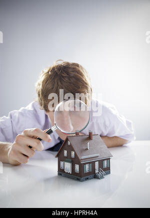 Jeune homme est titulaire d'une loupe sur une maison miniature. Banque D'Images