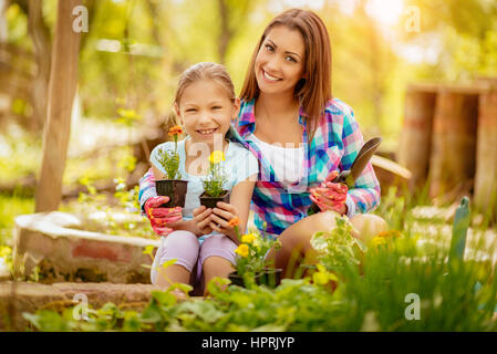 Belle jeune femme et petite fille planter des fleurs ensemble. En regardant la caméra. Banque D'Images