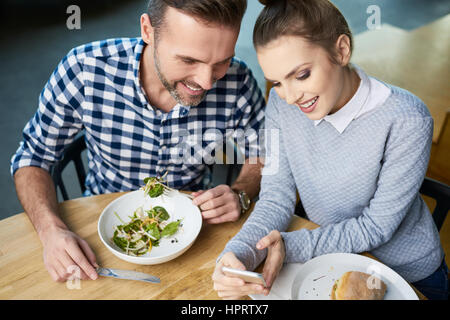 Au-dessus de la photo de l'homme et la femme adultes à manger à la table à l'écran du smartphone et souriant Banque D'Images