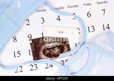Test de grossesse avec résultat positif, l'échographie de bébé et des vêtements pour nouveau-nés sur le calendrier, concept de l'extension de la famille et s'attendant pour bébé Banque D'Images