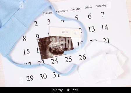 Test de grossesse avec résultat positif, l'échographie de bébé et des vêtements pour nouveau-nés sur le calendrier, concept de l'extension de la famille et s'attendant pour bébé Banque D'Images