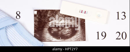 Test de grossesse avec résultat positif, l'échographie de bébé et des vêtements pour nouveau-nés sur le calendrier, concept de l'extension de la famille et s'attendant pour bébé Banque D'Images