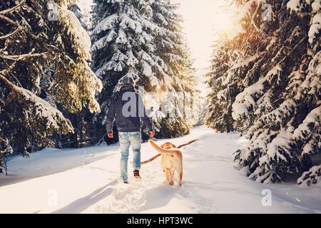 Voyage en hiver la nature. Jeune homme dans des vêtements chauds marche avec son labrador dans la forêt enneigée. Banque D'Images