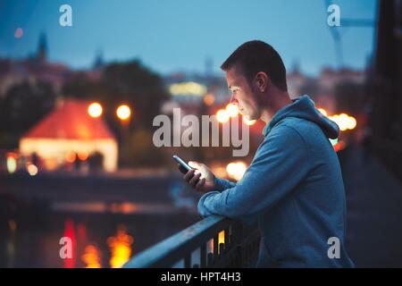 Seul dans la ville nocturne avec téléphone mobile. Bel homme de rêve message Lecture (ou à la recherche sur la vidéo) sur son smartphone. Banque D'Images