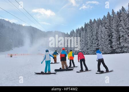 Groupe de snowboarders reposant sur la neige pendant l'écoute de l'instructeur Banque D'Images