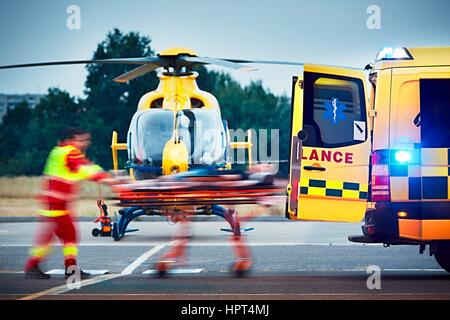 La coopération entre les services de secours aériens et les services médicaux d'urgence sur le terrain. Paramedic tire civière avec un patient à l'ambulance. Banque D'Images