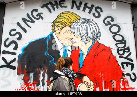 Bristol, Royaume-Uni. Feb 24, 2017. Une femme est photographié devant un nouveau morceau de street art avertissement au sujet de la mort de la NHS. Le travail d'art,une partie de 'Save the NHS' protester contre la diminution du financement accordé à l'ENM est apparu au cours des derniers jours à la Stokes Croft de la ville.La peinture montre le premier ministre et le Président peut l'emporter sur les baisers et les avertit qu'un lien trop étroit entre les deux pays après Brexit pourrait annoncer la fin de la NHS. Credit : lynchpics/Alamy Live News Banque D'Images