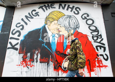 Bristol, Royaume-Uni. Feb 24, 2017. Un homme est photographié devant un nouveau morceau de street art avertissement au sujet de la mort de la NHS. Le travail d'art,une partie de 'Save the NHS' protester contre la diminution du financement accordé à l'ENM est apparu au cours des derniers jours à la Stokes Croft de la ville.La peinture montre le premier ministre et le Président peut l'emporter sur les baisers et les avertit qu'un lien trop étroit entre les deux pays après Brexit pourrait annoncer la fin de la NHS. Credit : lynchpics/Alamy Live News Banque D'Images