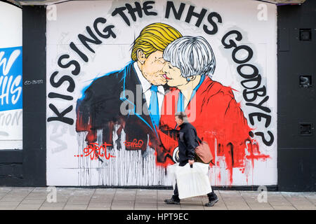 Bristol, Royaume-Uni. Feb 24, 2017. Un homme est photographié devant un nouveau morceau de street art avertissement au sujet de la mort de la NHS. Le travail d'art,une partie de 'Save the NHS' protester contre la diminution du financement accordé à l'ENM est apparu au cours des derniers jours à la Stokes Croft de la ville.La peinture montre le premier ministre et le Président peut l'emporter sur les baisers et les avertit qu'un lien trop étroit entre les deux pays après Brexit pourrait annoncer la fin de la NHS. Credit : lynchpics/Alamy Live News Banque D'Images