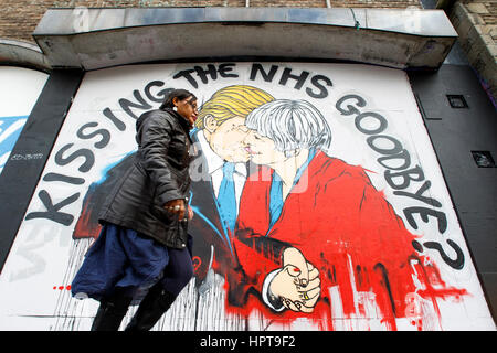 Bristol, Royaume-Uni. Feb 24, 2017. Une femme est photographié devant un nouveau morceau de street art avertissement au sujet de la mort de la NHS. Le travail d'art,une partie de 'Save the NHS' protester contre la diminution du financement accordé à l'ENM est apparu au cours des derniers jours à la Stokes Croft de la ville.La peinture montre le premier ministre et le Président peut l'emporter sur les baisers et les avertit qu'un lien trop étroit entre les deux pays après Brexit pourrait annoncer la fin de la NHS. Credit : lynchpics/Alamy Live News Banque D'Images