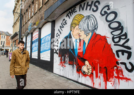 Bristol, Royaume-Uni. Feb 24, 2017. Un homme est photographié devant un nouveau morceau de street art avertissement au sujet de la mort de la NHS. Le travail d'art,une partie de 'Save the NHS' protester contre la diminution du financement accordé à l'ENM est apparu au cours des derniers jours à la Stokes Croft de la ville.La peinture montre le premier ministre et le Président peut l'emporter sur les baisers et les avertit qu'un lien trop étroit entre les deux pays après Brexit pourrait annoncer la fin de la NHS. Credit : lynchpics/Alamy Live News Banque D'Images