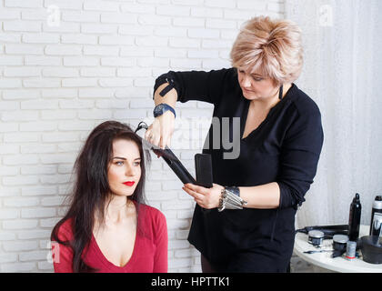 Coiffeur professionnel femme d'âge moyen avec des cheveux longs de redressage des fers de cheveux au salon de beauté. Jeune femme obtient ses cheveux à la péréquation. Styliste Banque D'Images