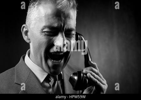 Bel homme tenant un récepteur téléphonique vintage sur fond sombre. Banque D'Images