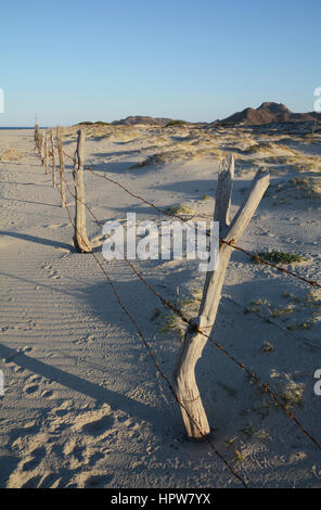 Un tir vertical d'une simple clôture sur un désert de sable. Un petit aperçu de l'océan est à l'arrière-plan. Banque D'Images