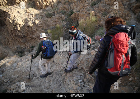Senior citizen les randonneurs sont soigneusement la descente d'une pente raide dans une gorge profonde. Le Canyon de Nahal ou Nahal Tze'elim, le désert de Judée, en Israël. Banque D'Images