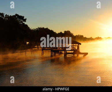 La lumière d'or et de l'eau quai en bois teintes de l'or, comme le lever du soleil hits Lake Chicot dans l'Est de l'Arkansas. Le brouillard entoure boat house et la surface du lac. Banque D'Images