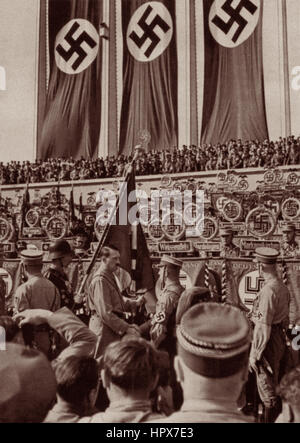 Adolf Hitler en 1934 à Nuremberg (Parti National Convention) shaking hands w/ soldat sur terrasse en pierre du hall d'honneur sous les bannières à croix gammée nazie. Banque D'Images