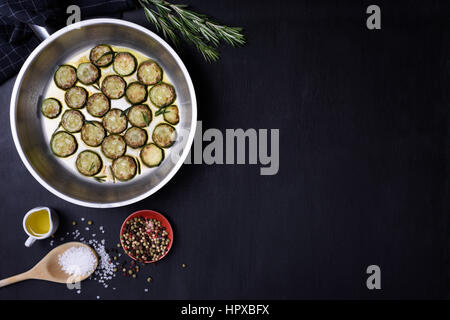 Les courgettes et romarin frit dans une casserole, salez et poivrez sur fond de bois sombre. Mise à plat, l'espace de copie. Plat végétarien. Banque D'Images