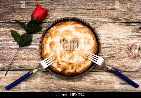 Tarte aux pommes avec un creux en forme de coeur et deux fourches sur une table en bois dans lequel il y a une rose rouge Banque D'Images