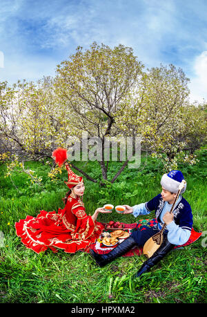 Couple en costume Kazakh assis au printemps fleurs jardin apple au picnic à Almaty, Kazakhstan, en Asie centrale Banque D'Images