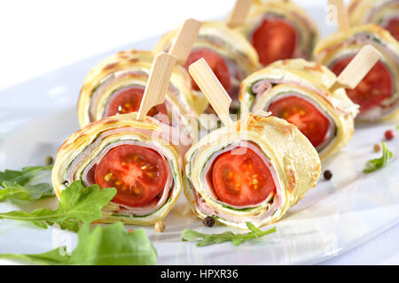 De délicieux amuse : Rouleaux de crêpes minces (crêpes) avec jambon, fromage à la crème, salade de roquette et tomates cerises Banque D'Images