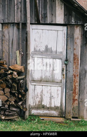 La porte de l'ancienne grange avec décollement de peinture blanche. Près de jeter les bois empilés dans un tas. Porte fermée sur le verrou. Banque D'Images