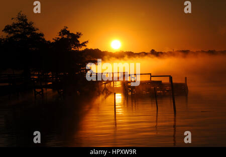 Matin d'or se lève sur le lac Chicot dans l'Est de l'Arkansas. Le brouillard s'élève de la surface calme de l'eau et la lumière silhouettes ancienne en bois dock. Banque D'Images