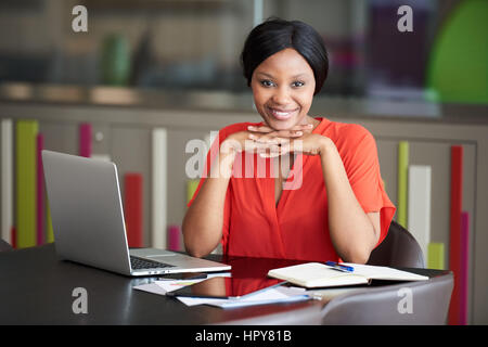 Young black female student smiling at the camera tout en soutenant sa tête avec ses mains qui sont asservis, assis à la conférence Banque D'Images