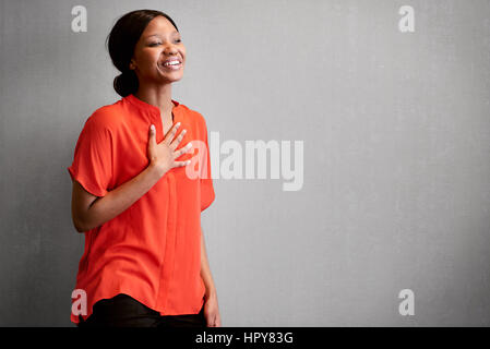 Femme noire de personne d'affaires occupé à rire avec une main contre sa poitrine tout en portant un chemisier orange colorés avec de l'espace pour copier du texte sur Banque D'Images