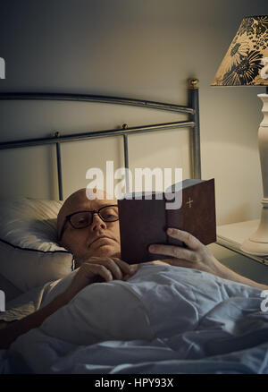 Middle aged man reading Bible on bed Banque D'Images