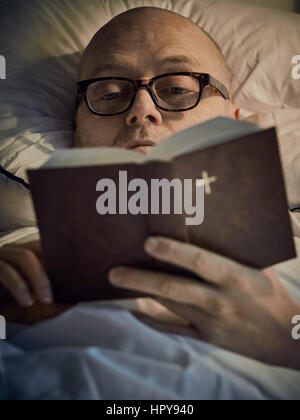 Middle aged man reading Bible on bed Banque D'Images