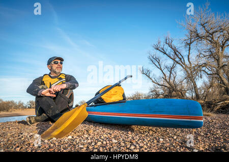 A senior male paddler est prendre du repos sur un gravelbar au cours de Stand up Paddling sur la rivière South Platte, saison froide scenery Banque D'Images