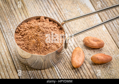 Cacao poudre dans une pelle à mesurer en métal contre bois grunge fond avec certains haricots crus Banque D'Images