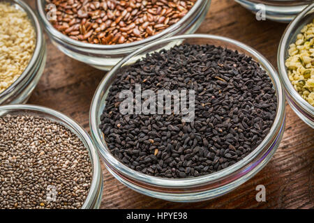 Les graines de cumin noir (Nigella Sativa) dans un petit bol avec du bois grange rustique contre chia et autres semences saines Banque D'Images