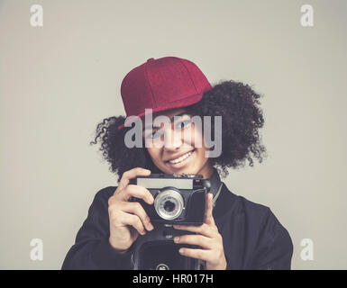 Portrait de l'Afrique de l'smileing jolie jeune femme hipster adolescente modèle avec appareil photo rétro rose portant un chapeau, veste en cuir noire. Fashion look. Banque D'Images